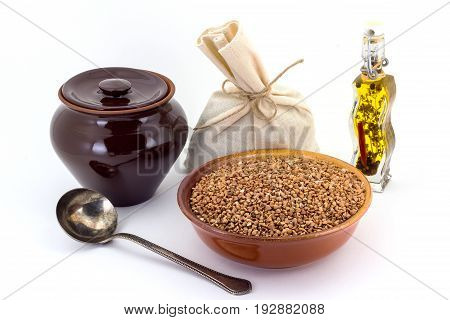 Still life of Buckwheat cereal in ceramic pial, ceramic pot, old spoon and canvas bag for cereals, oil with spices and seasonings, isolated on white background