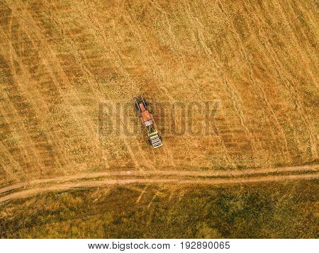 Aerial view of tractor making hay bale rolls in field after wheat harvest drone pov