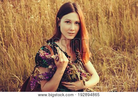 Happy red-haired woman with a bouquet of wildflowers. Village