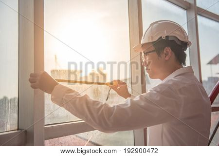Young Asian engineer man using tape measure (measuring tape) on window frame at construction site Length measurement tool or equipment for building construction working