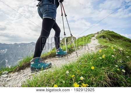 Woman running on narrow alpine mountain trail with hiking sticks.