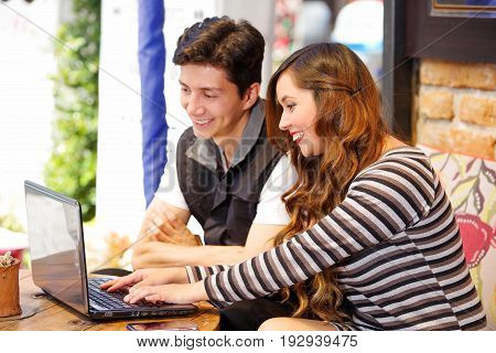Smiling happy couple at the bar spending time together, while they are working in his computer.