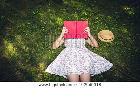 Woman reading a book and covering face outside on the grass