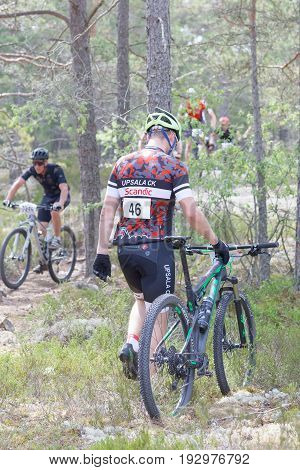 STOCKHOLM SWEDEN - JUNE 11 2017: Disappointed mountain bike cyclist leading the broken cycle in the forest at Lida Loop Mountain bike Race. June 11 2017 in Stockholm Sweden