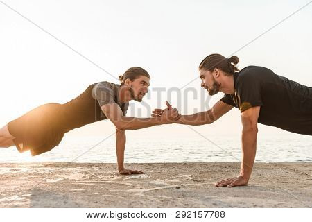Two twin brothers doing exercises at the beach together, doing push-ups, high five