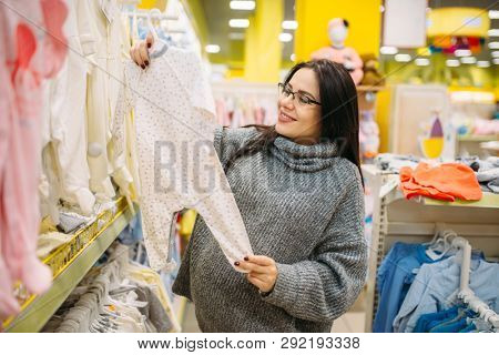 Happy future mother choosing clothes in the store