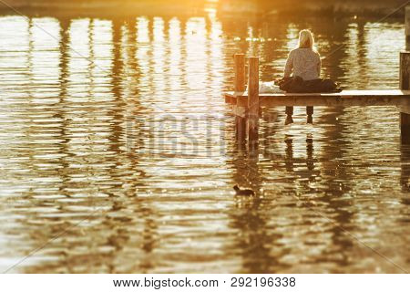 An image of a woman sitting on a wooden jetty at Starnberg Lake Tutzing Bavaria Germany