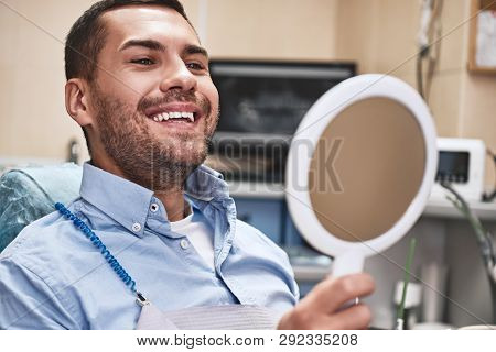 Your Smile Is Our Mission. Handsome Male Patient Looking At His Beautiful Smile Sitting At The Denta