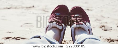 Feet Of Young Woman In Sport Footwear And Jeans Relaxing After Hiking On Sand Beach. Pov. Adventure 
