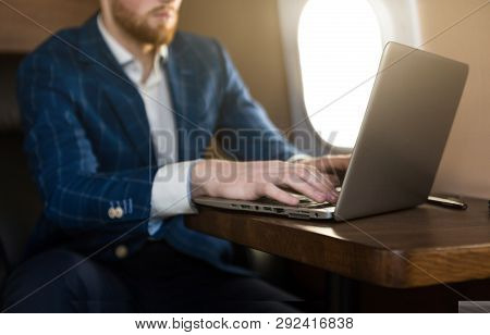 Attractive And Successful Businessman Working On A Laptop While Sitting In A Chair Of His Private Je
