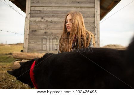 Happy Young Woman Plaing With Her Black Dog In Fron Of Old Wooden House. Girl Tries A Hat To Her Dog