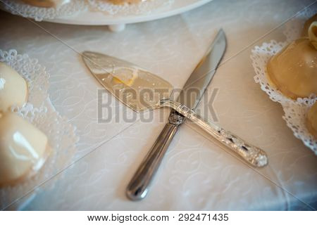 Knife And A Cake Cutter On A Wedding Table. Silver Cake Servers For Cookies On White Tablecloth. Clo
