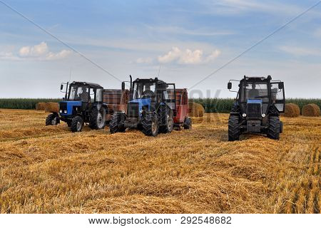 Three Wheeled Tractors With Roll Balers On A Sloping Wheat Field