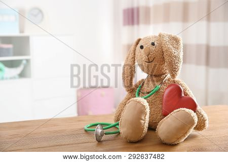 Toy Bunny, Stethoscope And Heart On Table Indoors, Space For Text. Children's Doctor