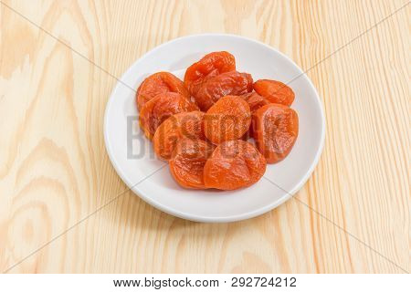 Dried Apricots On The White Saucer Close-up On A Light Colored Wooden Surface