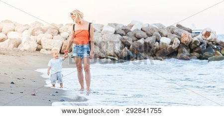 Woman Playing With Her Baby Outside Against The Sea. The Concept Of A Happy Full-fledged Family Life