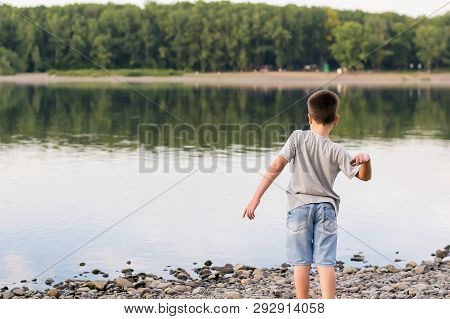 A Child, A Teenager, On A Stony Shore Throws Stones Into The River, Lake