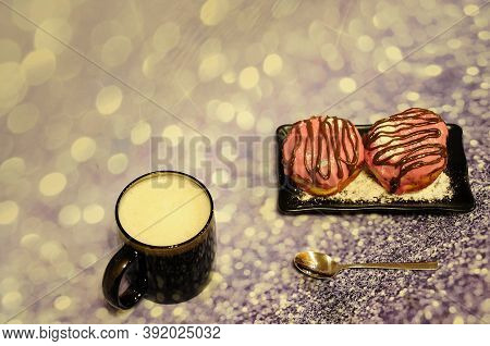 Cup Of Cappuccino And A Plate With Two Donuts In Pink Glaze With Chocolate And Powdered Sugar On A G