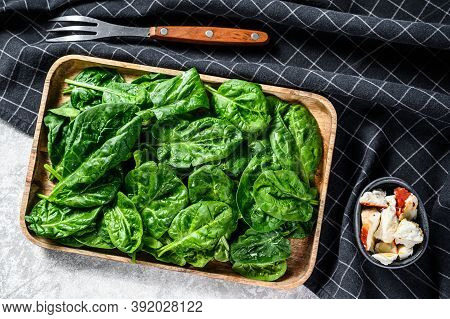 Fresh Spinach Salad In A Wooden Bowl With Goat Cheese. Gray Background. Top View