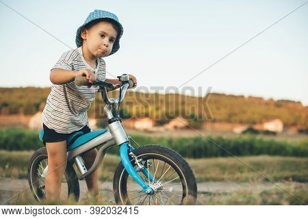 Concentrated Caucasian Boy With Blue Hat And Bike Looking Somewhere In A Field During A Summer Walk