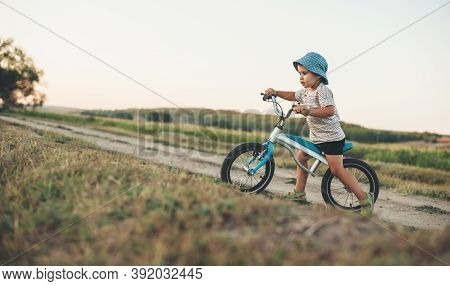 Side View Photo Of A Caucasian Boy With Blue Hat Riding A Bike On A Country Road