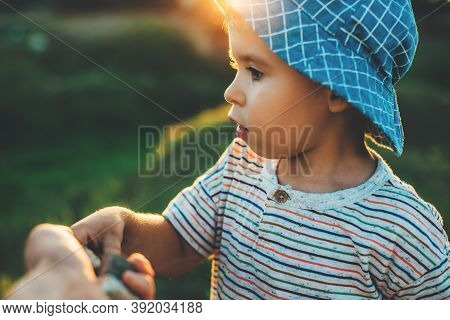 Close Up Photo Of A Caucasian Small Boy With A Blue Hat Taking Something From His Parents Hand While