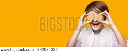 Smiling Caucasian Boy Is Covering His Eye With Sliced Lemon Pieces Posing On A Yellow Wall With Free
