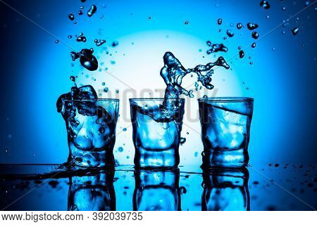 Strong Alcoholic Drink In Dammed Glasses With Ice On A Black Reflective Background. Splashes On A Bl