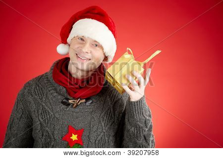 Portret van gelukkig man in Santa cap met geschenkdoos door zijn oor kijken camera