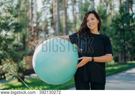 Positive Brunette Woman Leads Active Lifestyle Holds Fitness Ball Poses Against Forest Background Dr