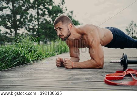 Muscular Bodybuilder Stands In Plank Pose Demonstrates Endurance Has Strong Biceps Poses Outdoor Has