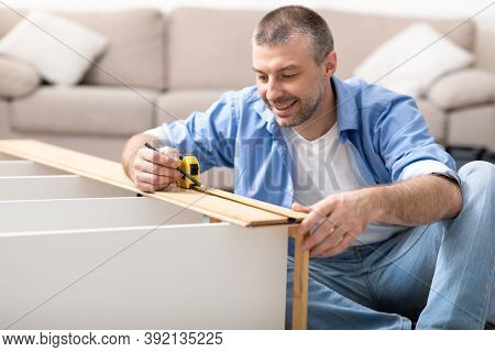 Furnishing House. Man Assembling Shelf Using Self-assembly Kit Installing New Furniture At Home, Sit