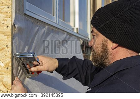 The Worker Fixes The Windproof Membrane With A Stapler