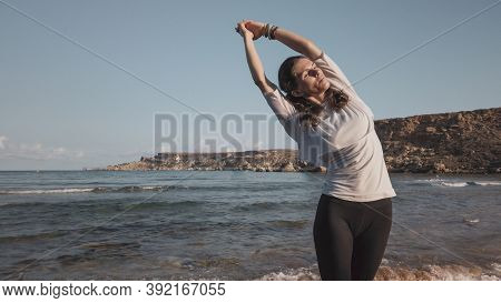 Young Caucasian Brunette Woman Doing Youga On The Sandy Beach In The Morning. High Quality Photo