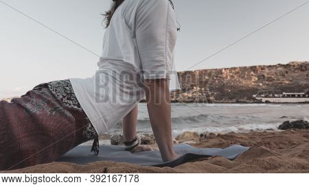 Young Caucasian Brunette Woman Doing Youga On The Sandy Beach In The Morning. High Quality Photo