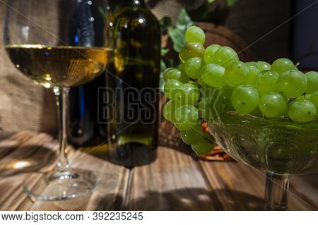 Two Bottles Of Red And White Wine On A Wooden Table With A Bunch Of Grapes And A Glass On A Thin Ste