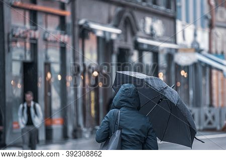 Rear View Of An Unrecognizable Woman In A Dark Winter Insulated Jacket With A Hood And An Umbrella I