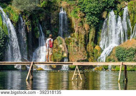 Kravica, BiH - August 31, 2019: Unidentified tourist stands on the wooden bridge in front of beautiful Kravica waterfall in Bosnia and Herzegovina. Beautiful cascade waterfall in forest
