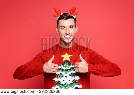 Front View Of Happy Young Adult Man With Headband Showing Thumbs Up Isolated On Red