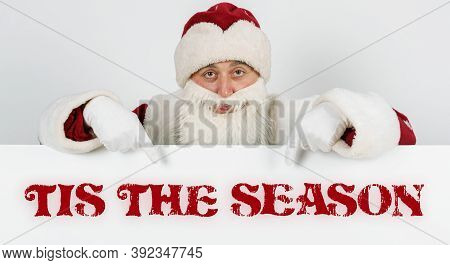 New Year And Christmas Concept. Santa Claus Points His Fingers At The Board With The Text - Tis The 