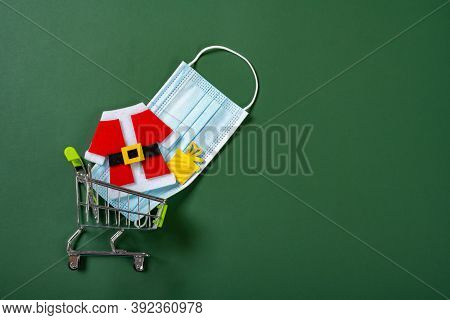 Shopping Cart With Medical Mask And Christmas Decorations On Green Background