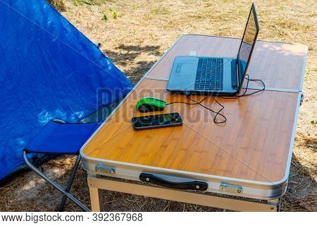 Laptop With Computer Mouse And Smartphone On A Folding Picnic Table In A Camping. Working While Trav