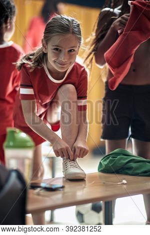 A little girl posing for a photo at the locker room while preparing for a training. Children team sport