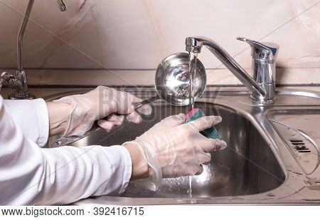 Woman's Hands With Gloves Washing Dish With Fresh Water At Kitchen Faucet Over The Metal Sink. Human