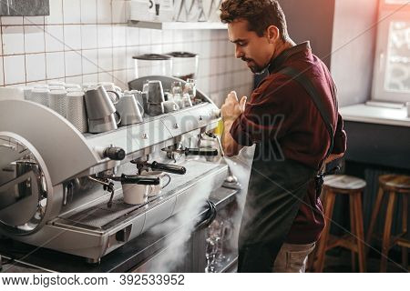 Side View Of Bearded Man In Apron Turning On Steam On Coffeemaker While Brewing Coffee During Work I