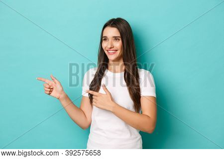 Portrait Of Attractive Caucasian Woman In White T-shrit, Looking And Pointing Fingers Left, Smiling 