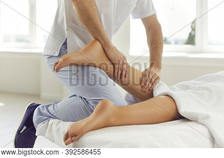 Physiotherapist Or Reflexologist Massaging Young Womans Calf Muscle In Wellness Center