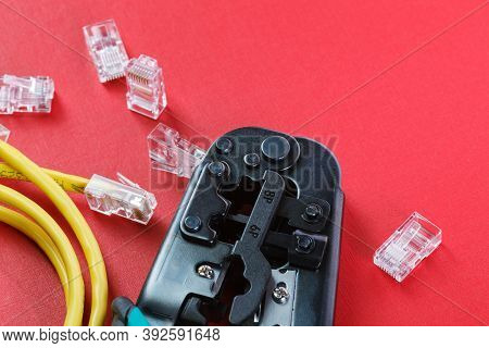 Computer Network Laying Concept. Crimper Tool And Transparent Connectors Connectors On Red Backgroun
