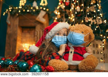 Portrait Of Cutel Little Child Girl In Medical Mask Playing With Taddy Bear, New Year Holiday Concep
