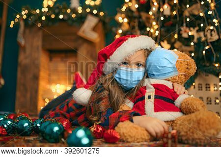 Portrait Of Cutel Little Child Girl In Medical Mask Playing With Taddy Bear, New Year Holiday Concep